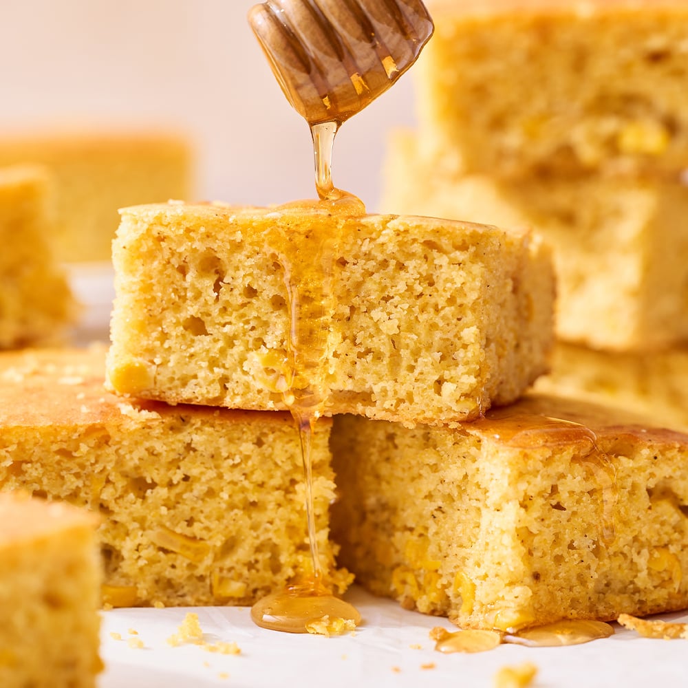 pieces of cornbread stacked on top of each other, with a drizzle of honey being poured over the top