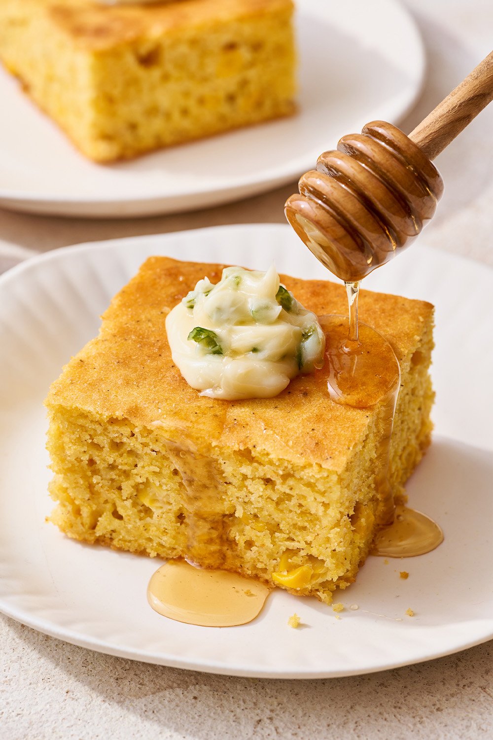 slice of cornbread on a plate with jalapeno butter piped on top, with honey being drizzled on top