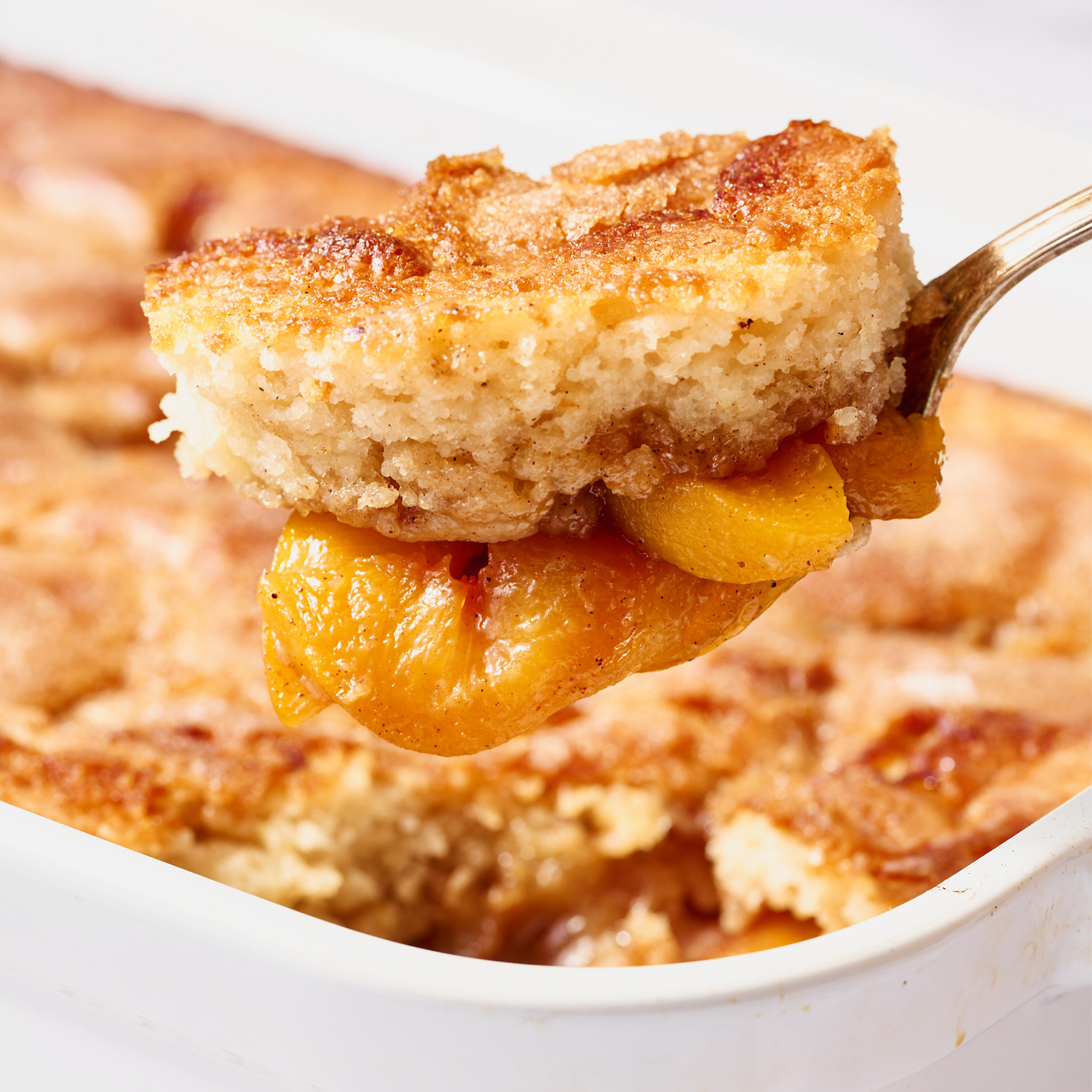 spoon lifting peach cobbler from baking dish