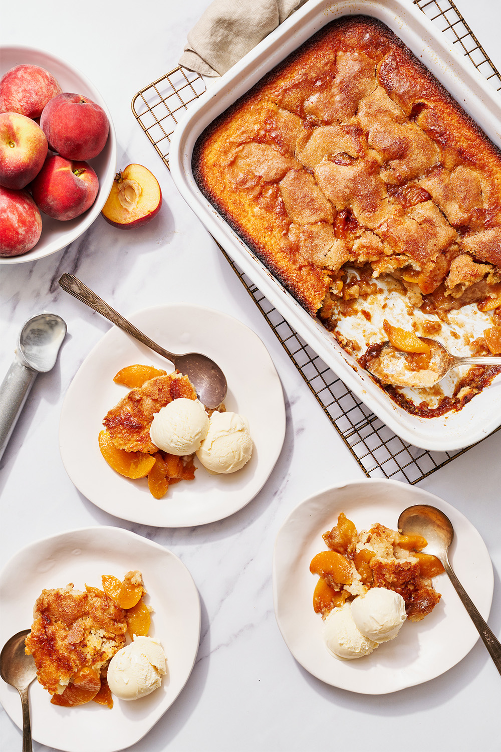 peach cobbler being served from a dish onto individual plates, topped with vanilla ice cream