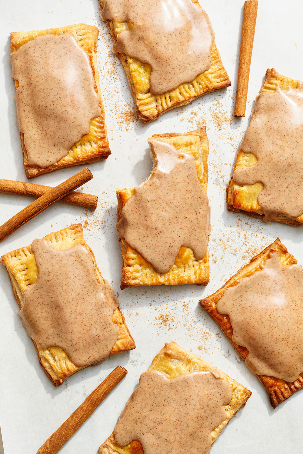 copycat frosted brown sugar cinnamon pop tarts on parchment paper with cinnamon sticks