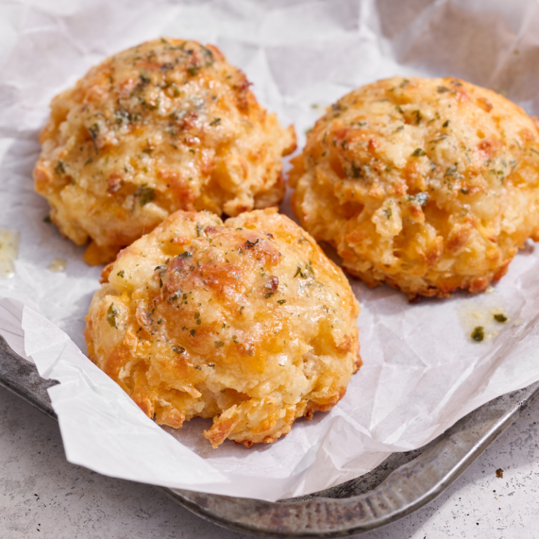 three cheesy garlic biscuits on a parchment-lined baking tray, ready to serve.