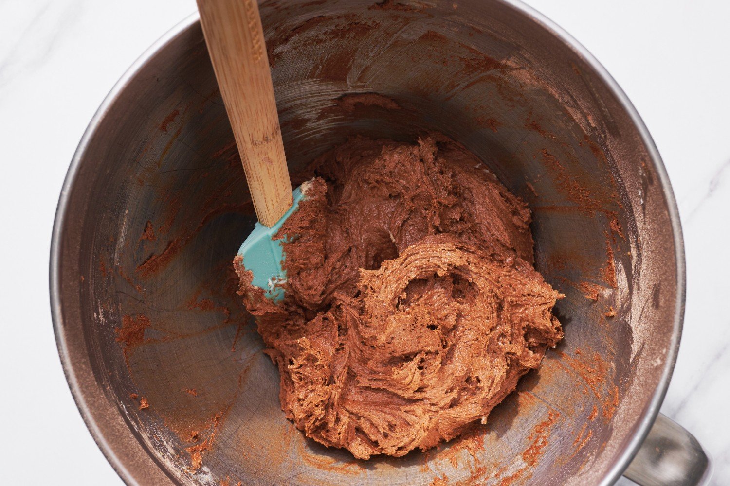 a metal mixing bowl with cookie dough and a spatula inside.