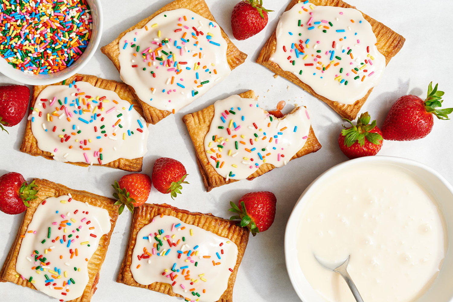 several poptarts on a white background with some fresh strawberries in between.