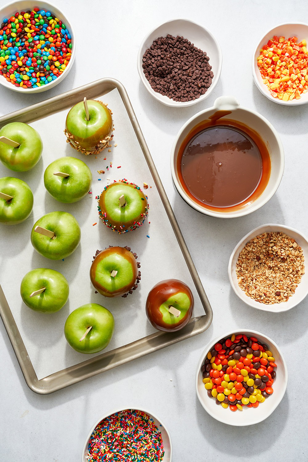 apples on a tray with bowls of toppings and the bowl of warm caramel nearby, ready to dip.