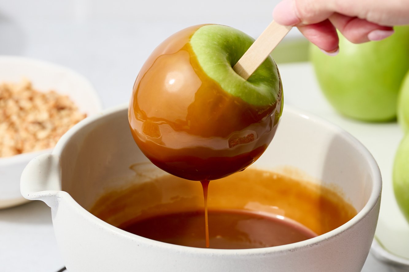 an apple being dipped into a bowl of warm caramel.