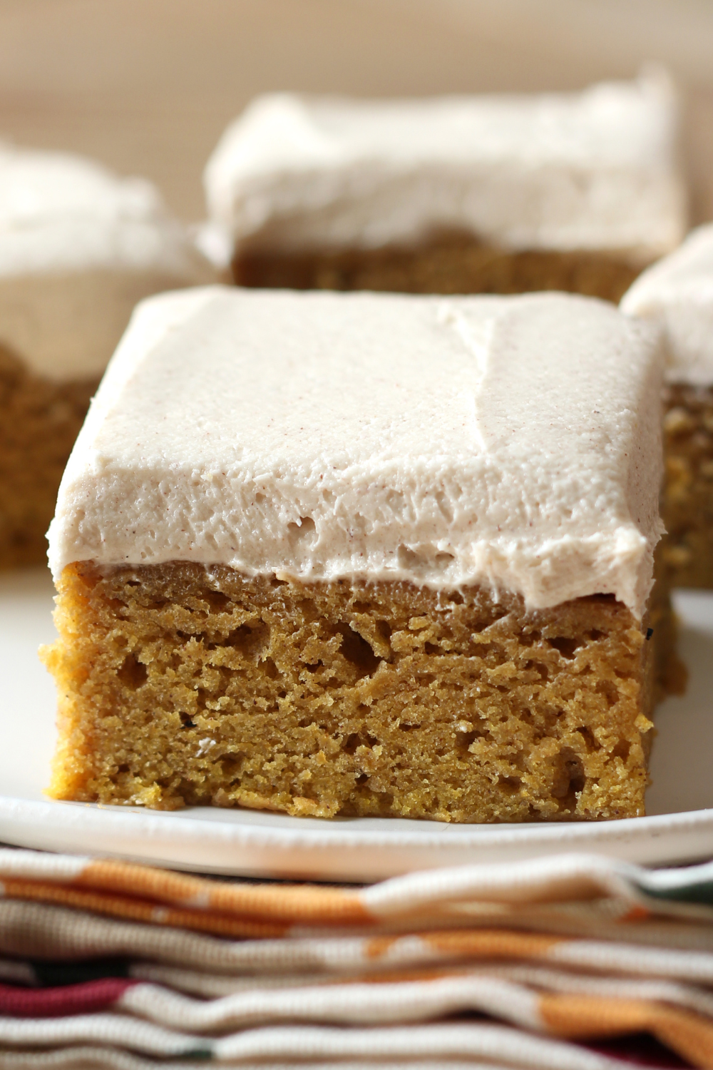 a close-up photo of a slice of pumpkin bar with brown sugar frosting sitting on a plate, with more bars behind