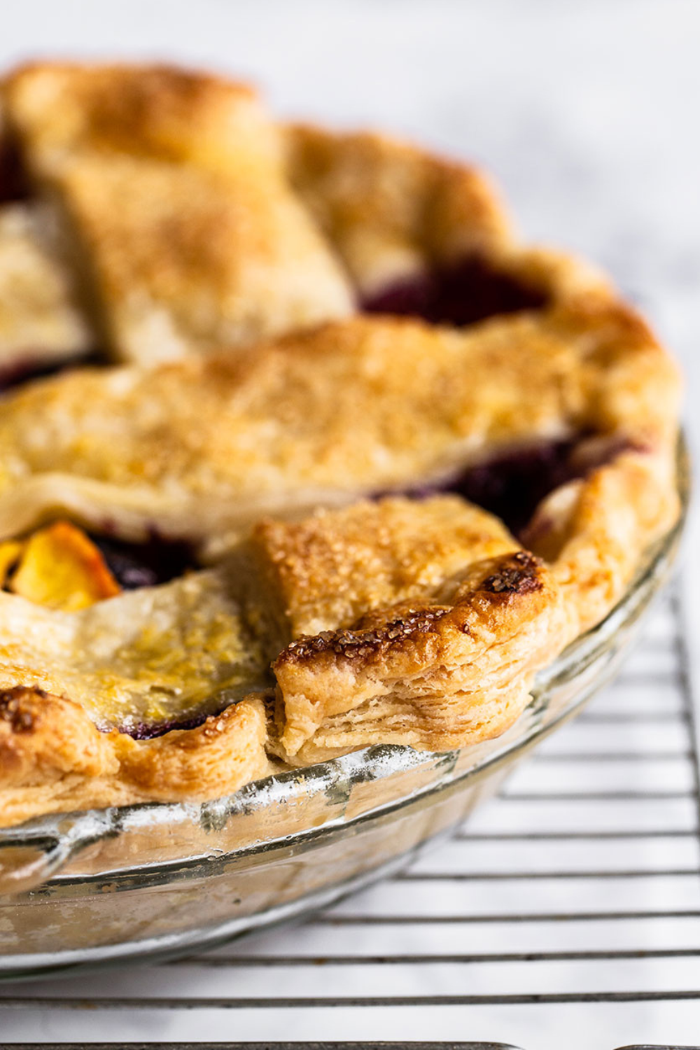 a baked blueberry peach pie topped with a visibly flaky, golden brown lattice pie crust.