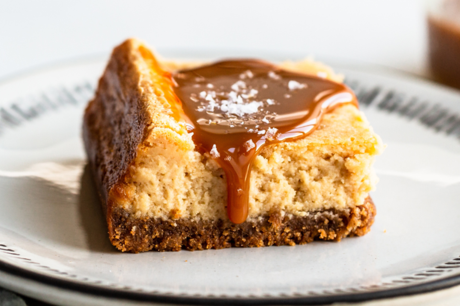 a salted caramel cheesecake bar on a plate, covered with gooey caramel sauce, ready to serve