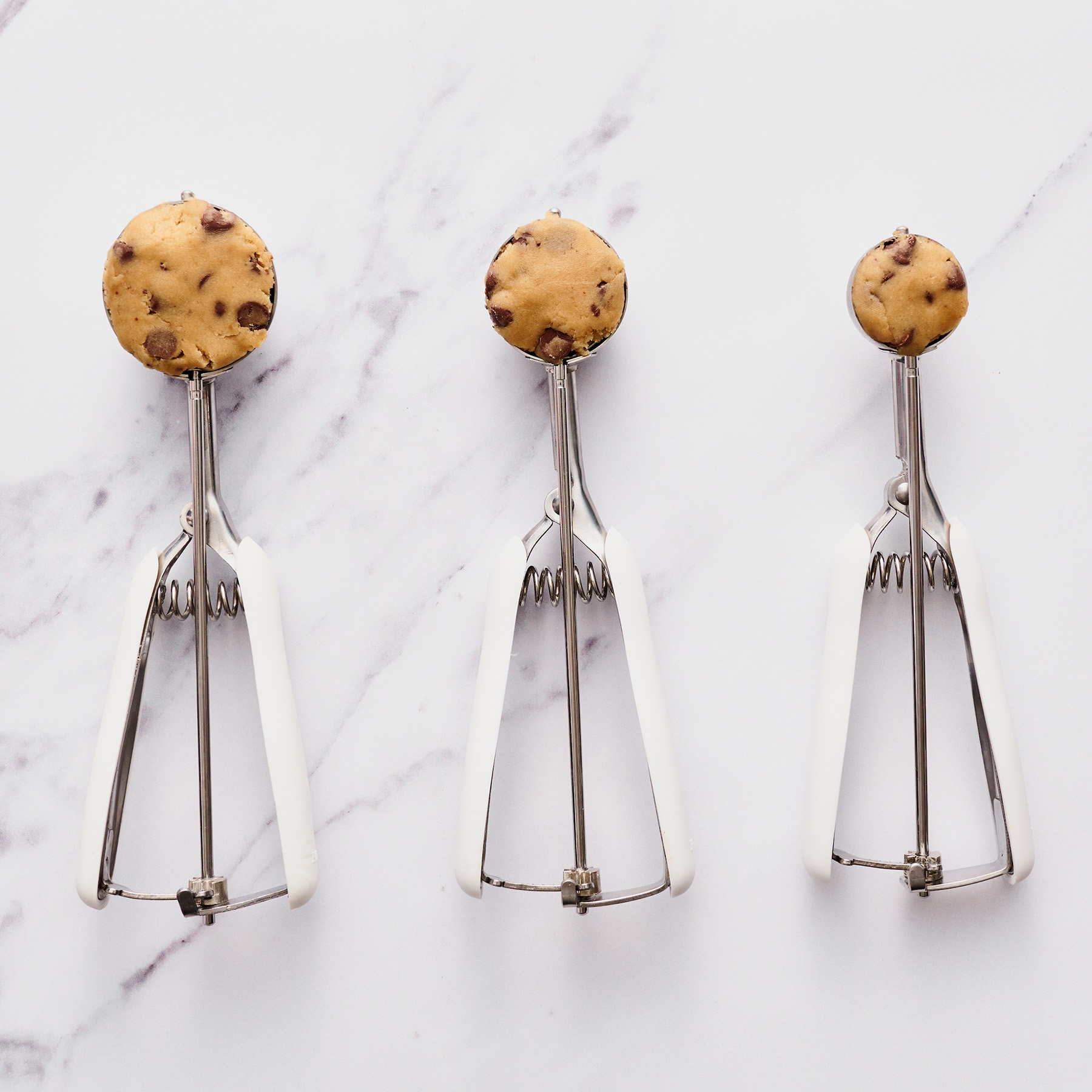 three different sizes of cookie scoops filled with cookie dough
