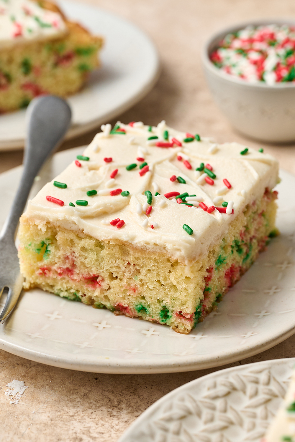 a slice of iced cake with sprinkles, on a plate with a fork to serve.