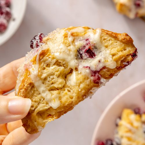 hand holding a cranberry orange scone with icing to show flaky layers