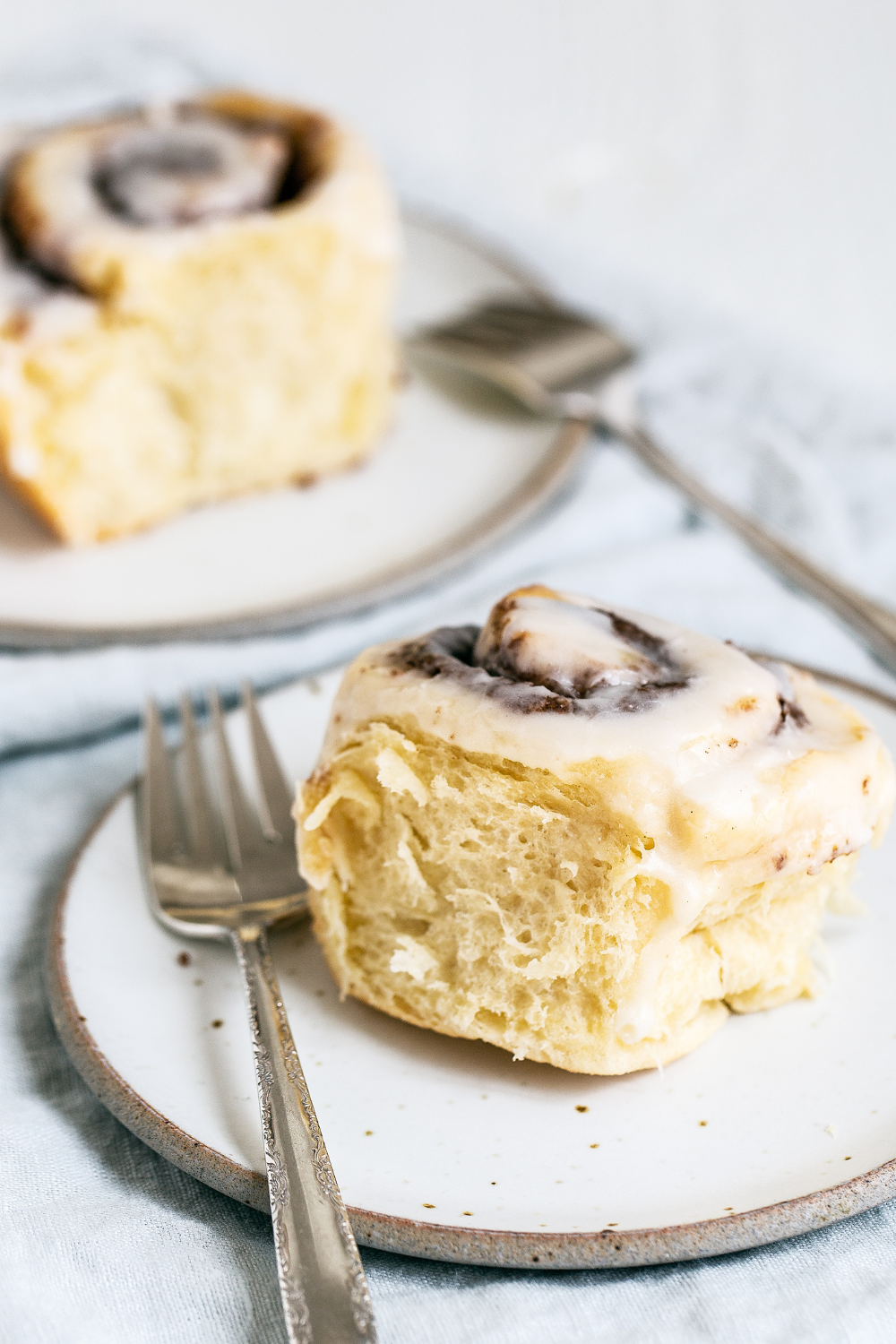 two cinnamon rolls sitting on plates with forks, ready to serve.