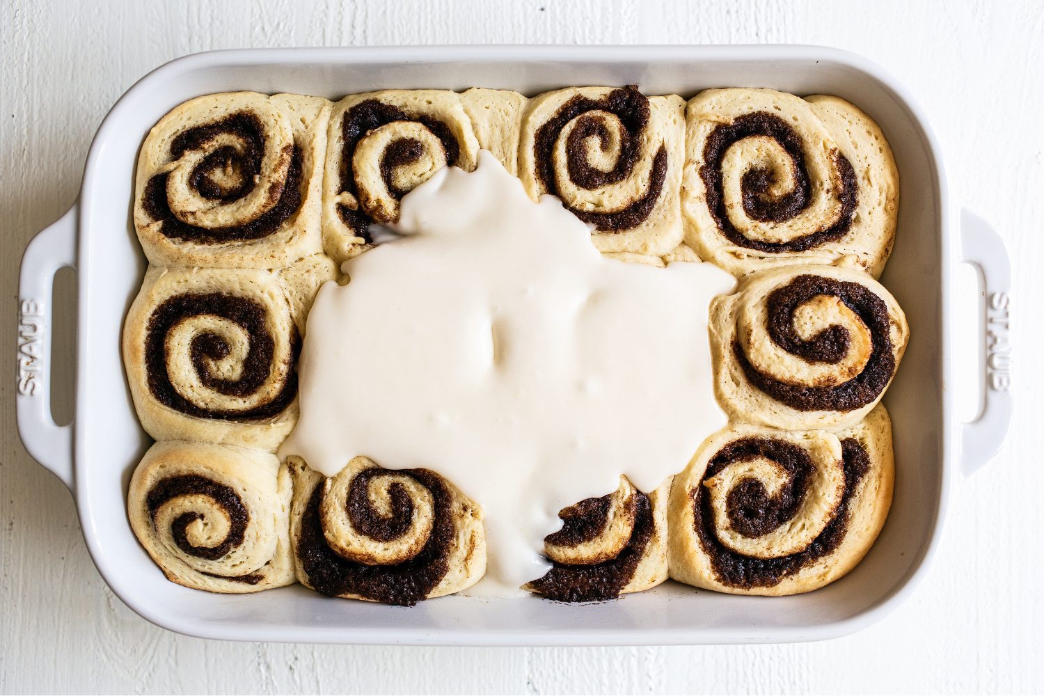 baked cinnamon buns being flooded with flowing white icing.