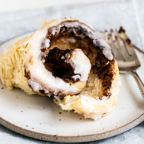a cinnamon rolls with a bite taken out, sitting on a plate beside a fork.