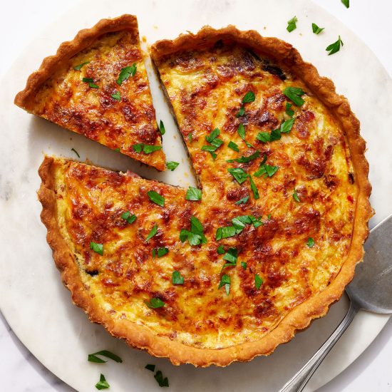 cheesy quiche lorraine on a marble platter with a slice of quiche taken out