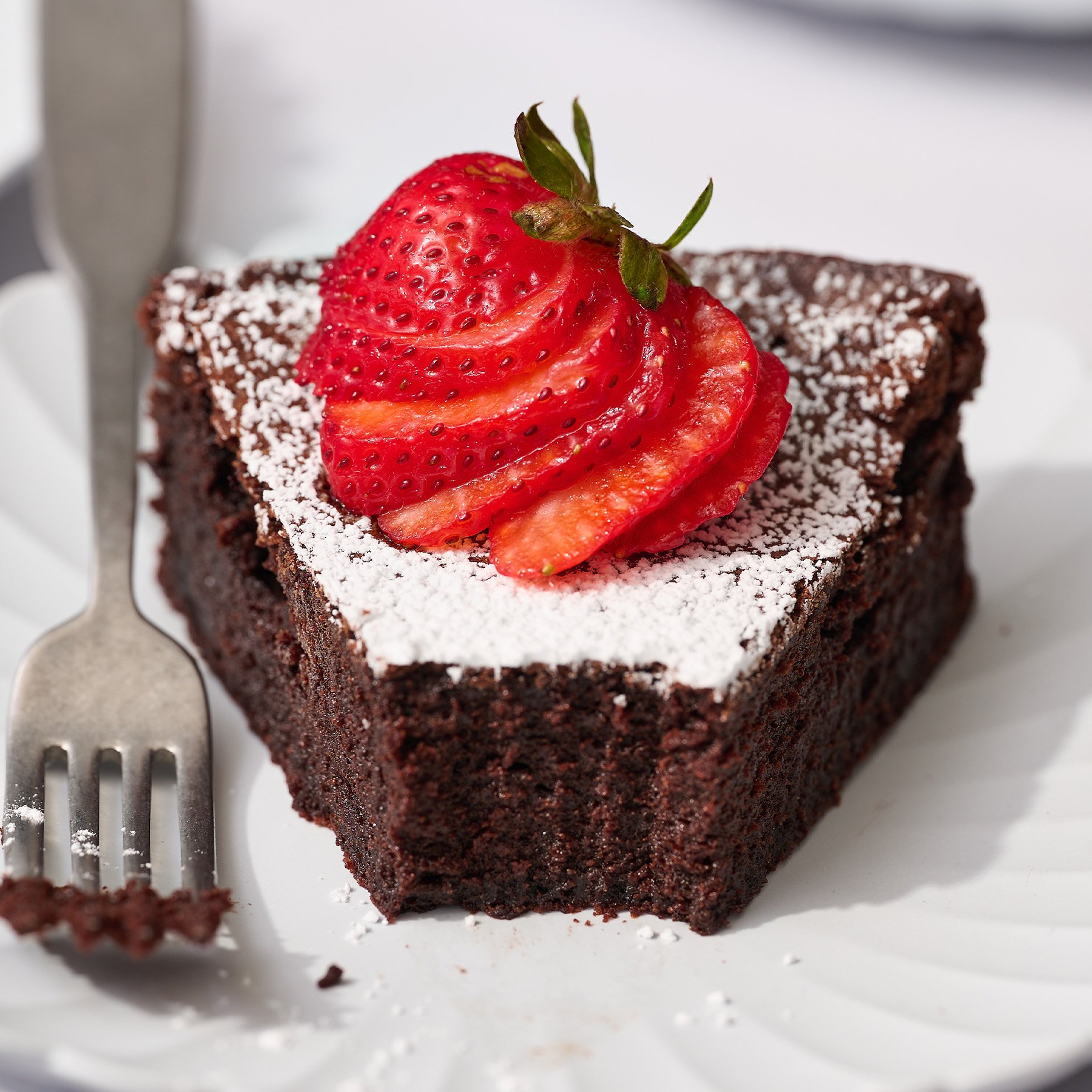 fudgy flourless chocolate cake recipe on a plate with a bite taken out