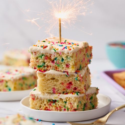 three slices of funfetti cake stacked on a small white plate, with a lit candle on top.