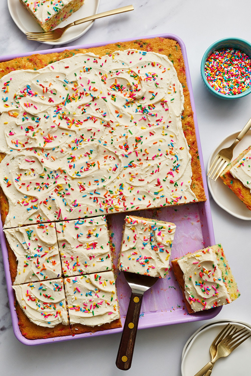 the funfetti sheet cake in a purple baking pan, being sliced up to serve.