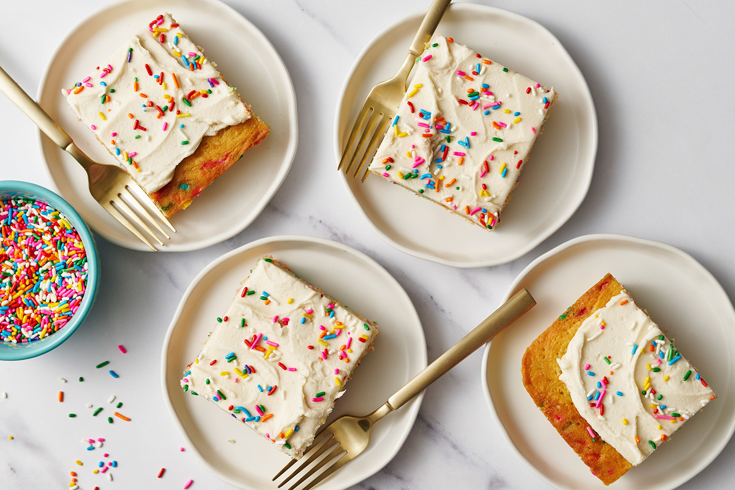slices of funfetti cake on white plates with forks to serve.