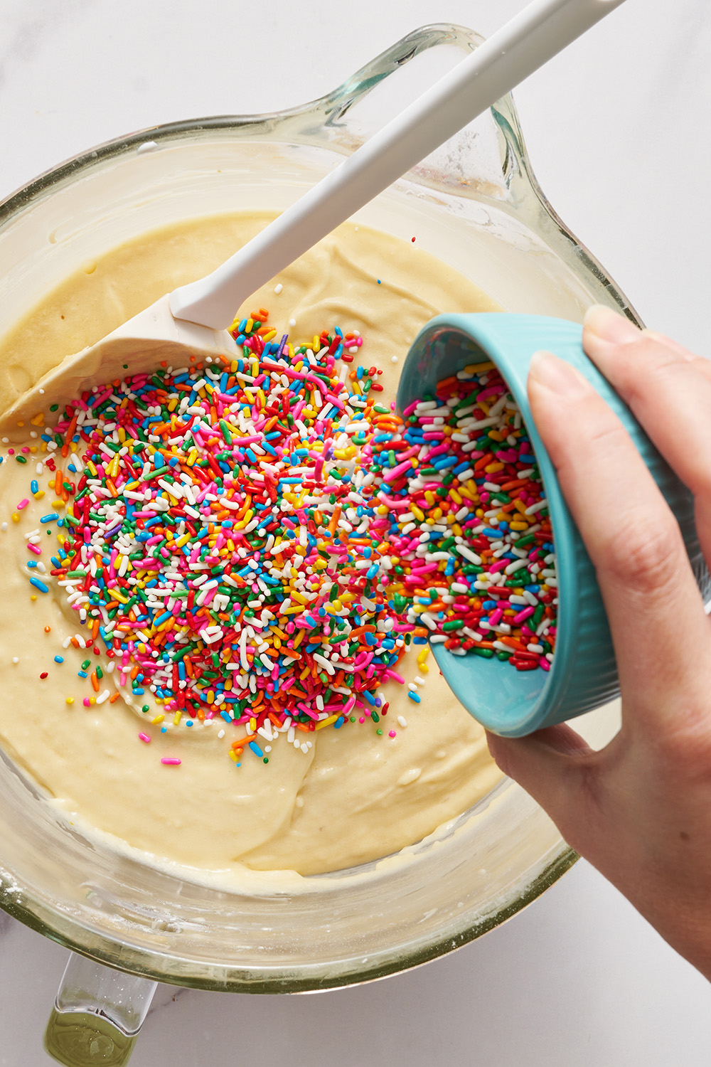 a hand pouring the sprinkles into the cake batter.