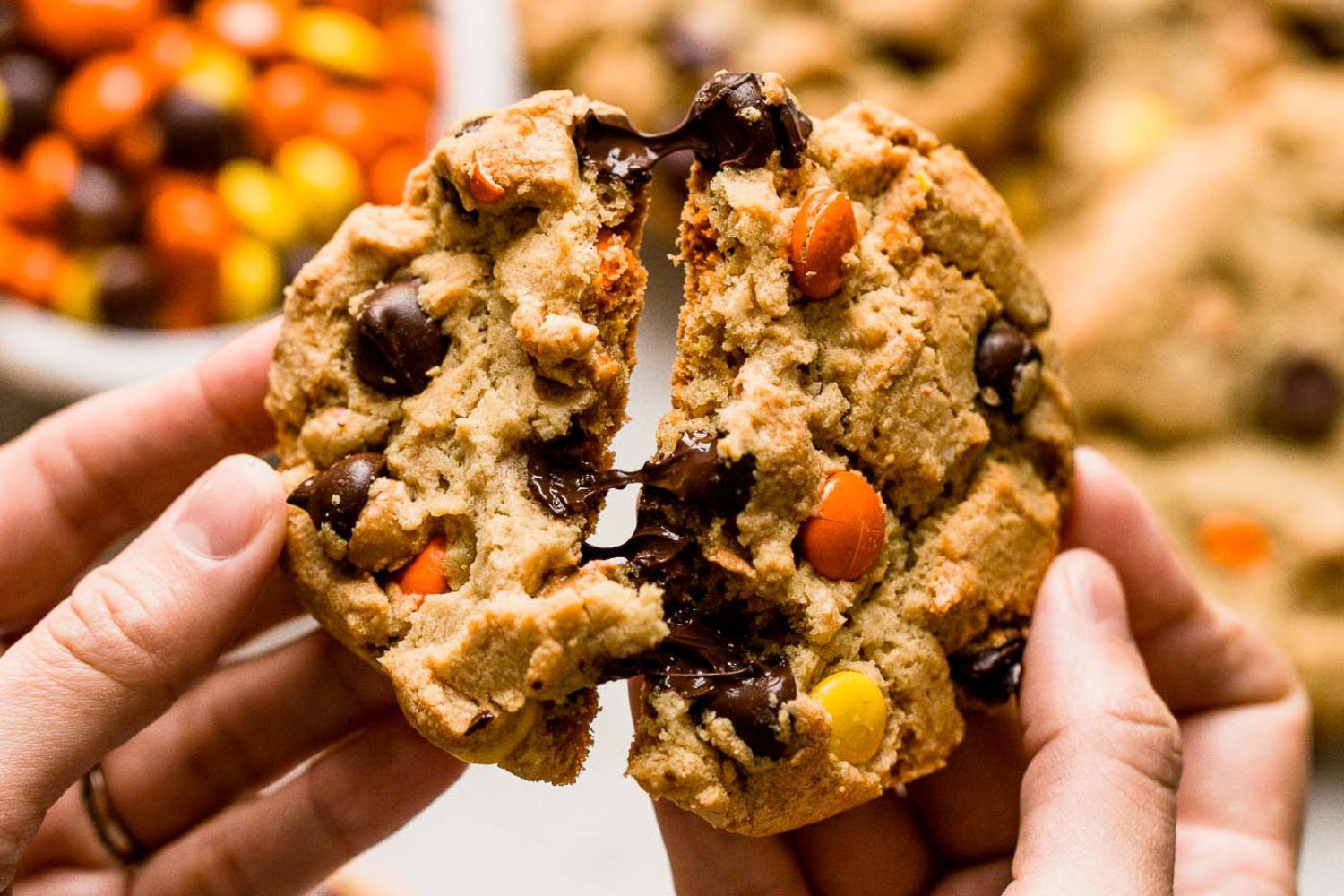 hands breaking a warm cookie in half, with gooey chocolate chips pulling between the halves.