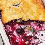 baking dish of blueberry cobbler with blueberry filling and serving spoon in the dish