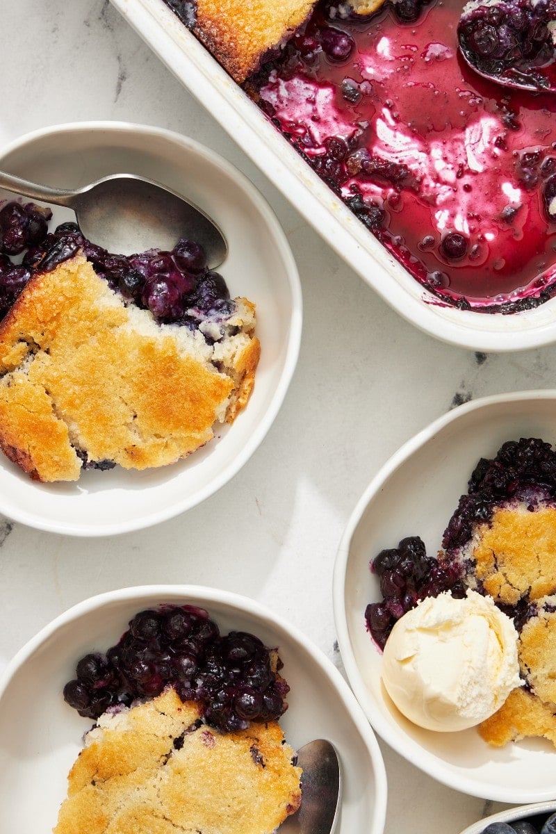 Overhead of warm blueberry cobbler scooped into bowls with vanilla ice cream on top