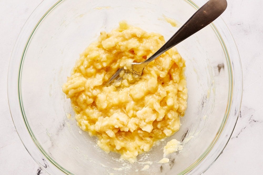 mashed banana in a glass bowl with a fork, ready for banana bread