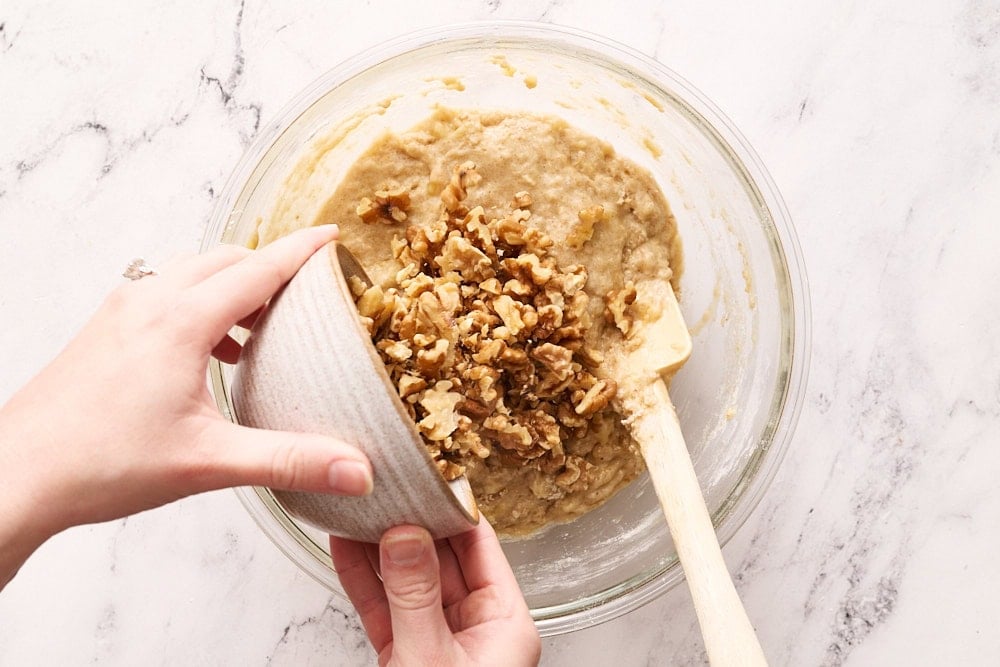adding nuts to banana bread batter in a glass bowl