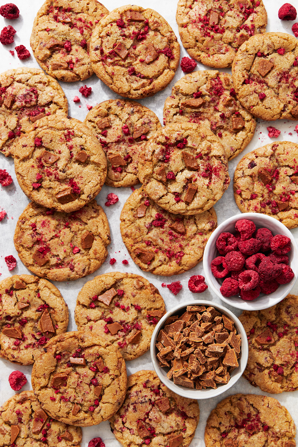 caramelized white chocolate cookies, with small bowls of freeze-dried raspberry pieces and chopped caramelized white chocolate around the cookies
