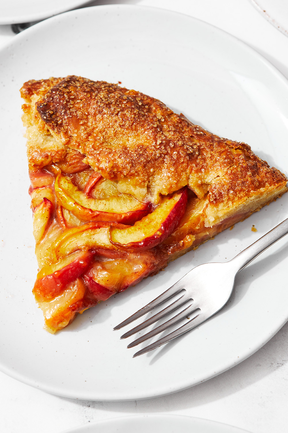 slice of peach galette on a white plate with a fork beside it