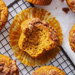 pumpkin streusel muffin with a bite taken out on a wire rack surrounded by other homemade pumpkin muffins