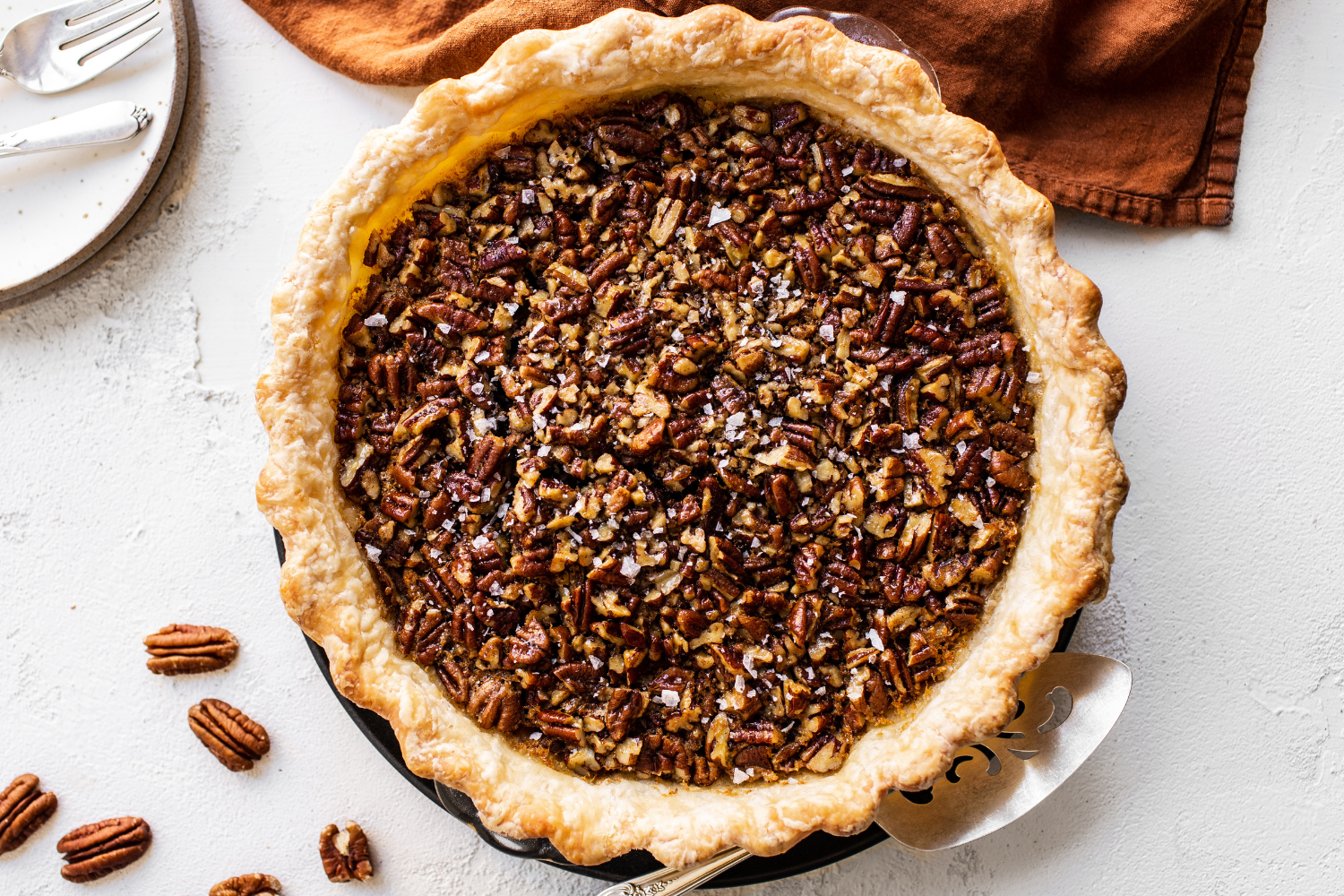 the perfect elevated pecan pie for friensgiving, unsliced in a pie pan, surrounded by pecans. 
