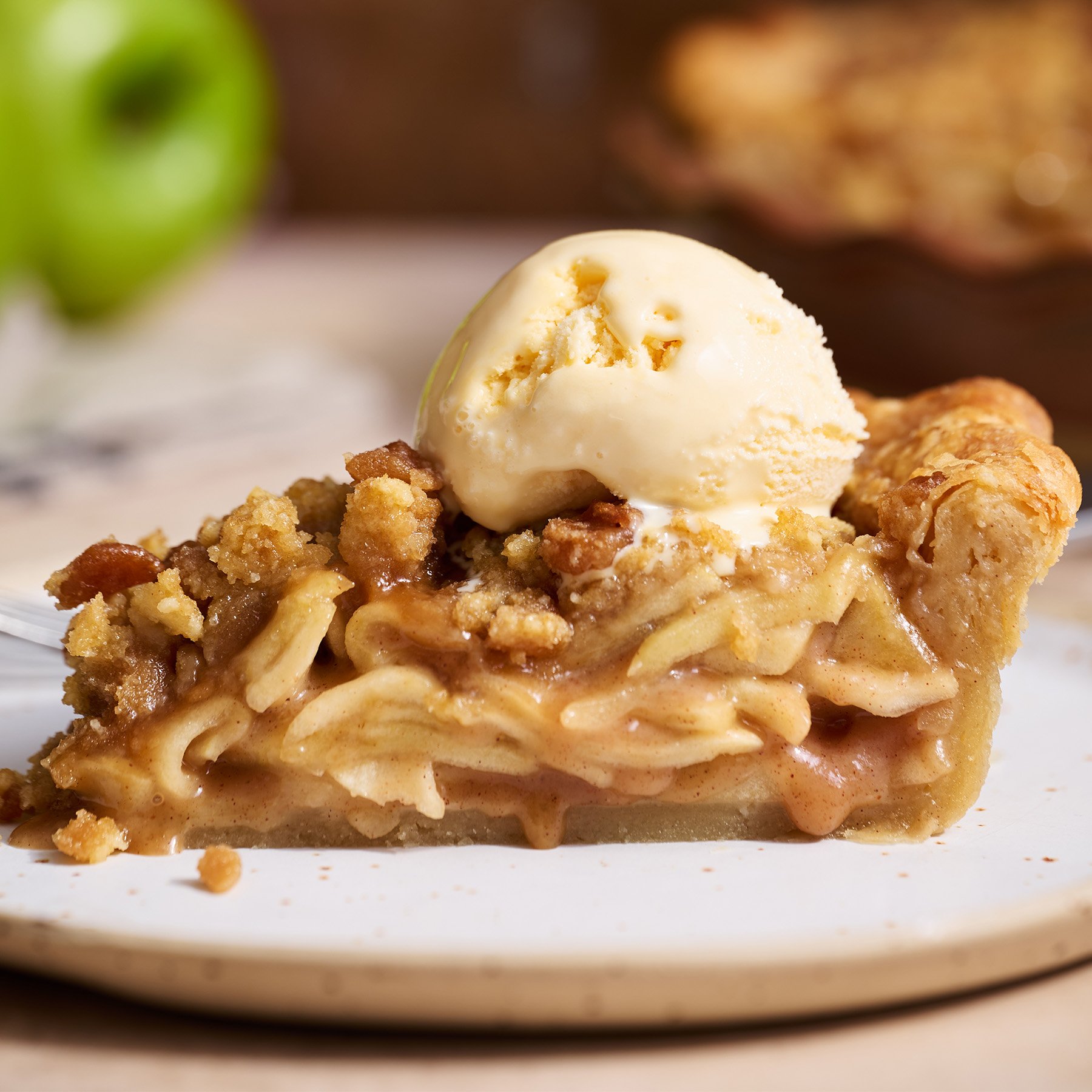 slice of homemade apple streusel pie on a plate with a scoop of vanilla ice cream on top