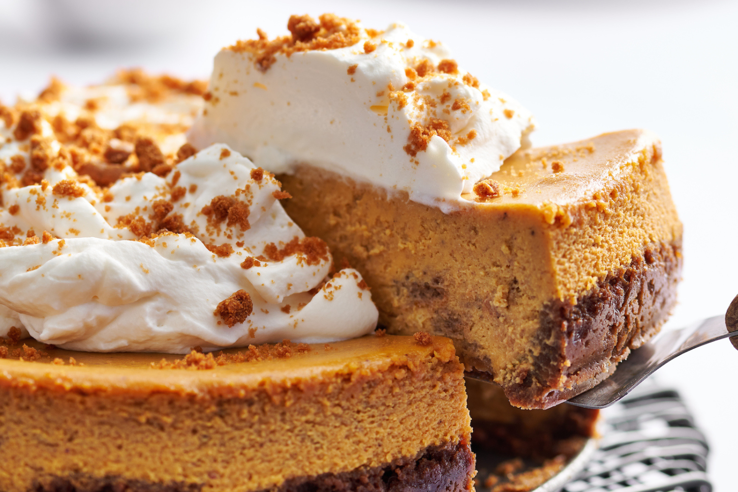 pumpkin cheesecake, topped with whipped cream, with a slice being cut and removed to serve.