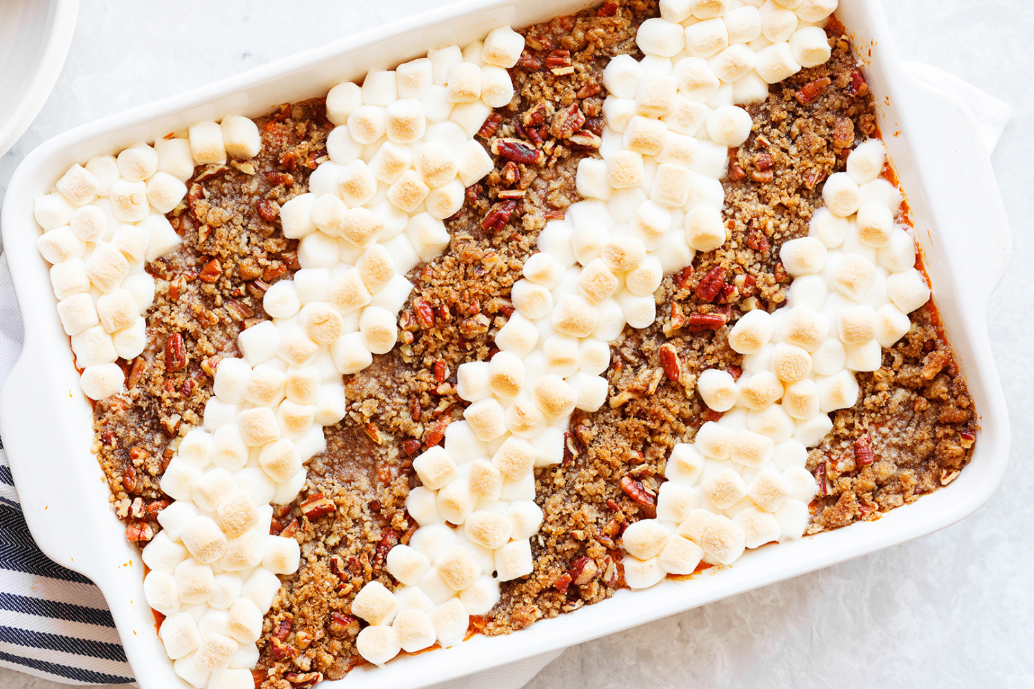 sweet potato casserole in a ceramic casserole dish, alternatingly topped with mini marshmallows and pecans.