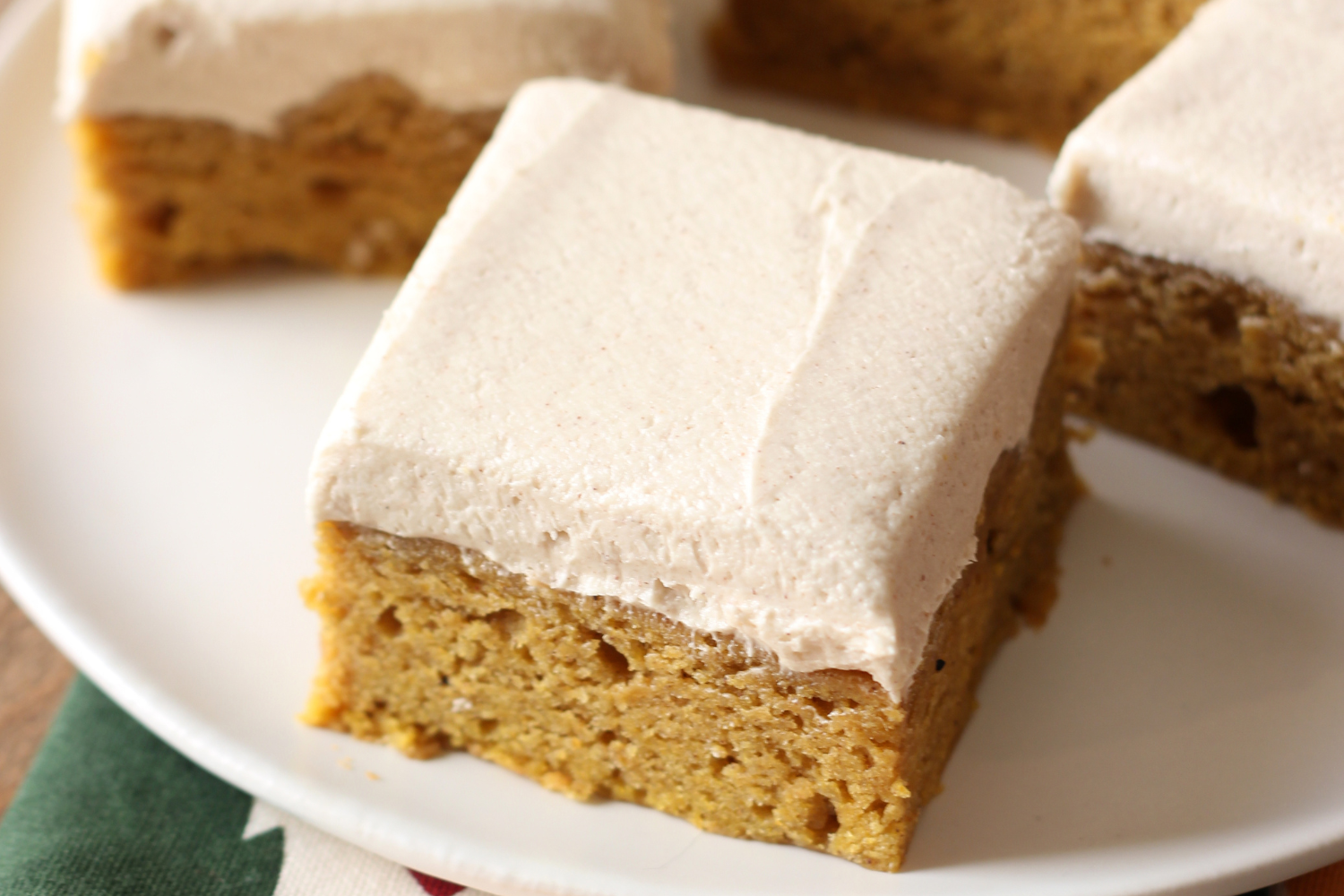 a slice of pumpkin bar with a thick layer of brown sugar frosting on top, sitting on a plate, with more bars behind.