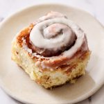 a gooey iced cinnamon roll on a small plate on a marble countertop