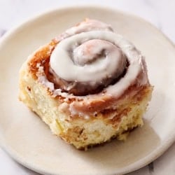 a gooey iced cinnamon roll on a small plate on a marble countertop