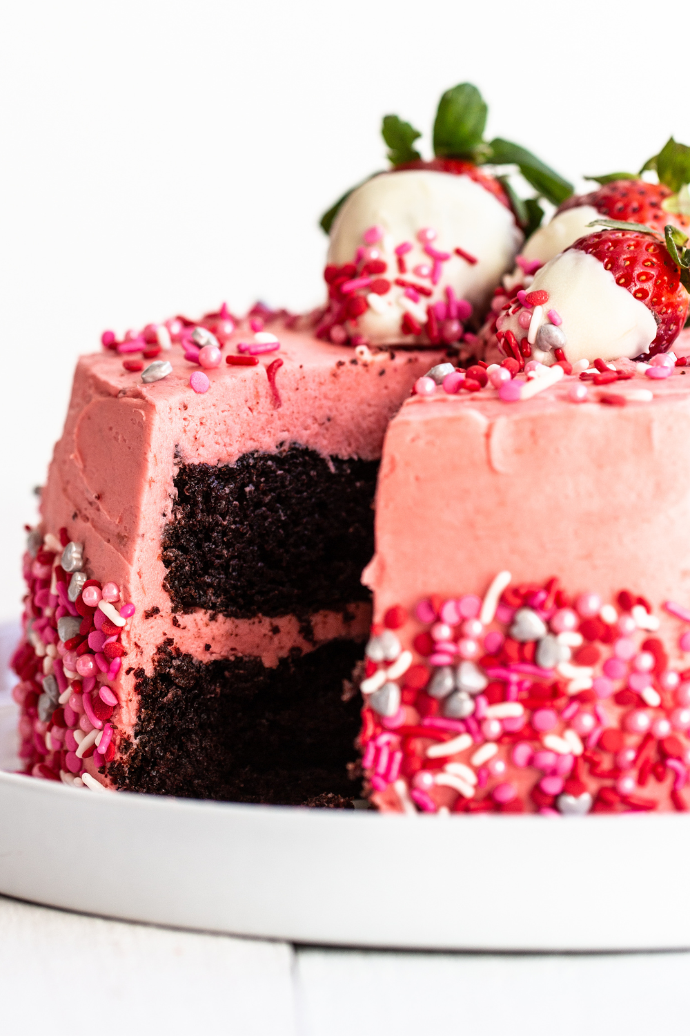 Valentine's Cake has two layers of chocolate sponge cake, sandwiched together with strawberry buttercream and iced in the same frosting, topped with chocolate-covered strawberries.
