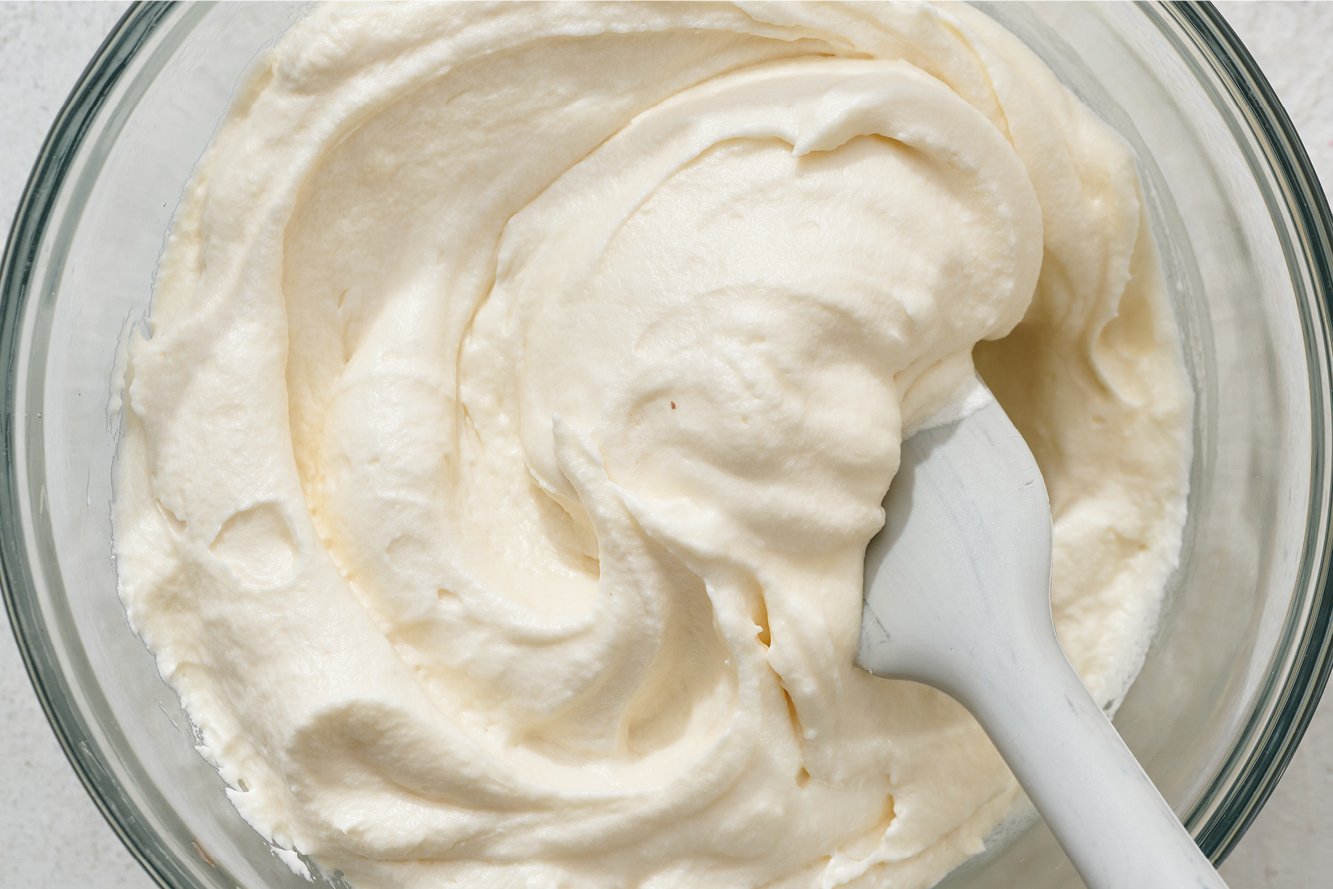 a glass bowl filled with cream cheese frosting, an a spatula in the middle. 