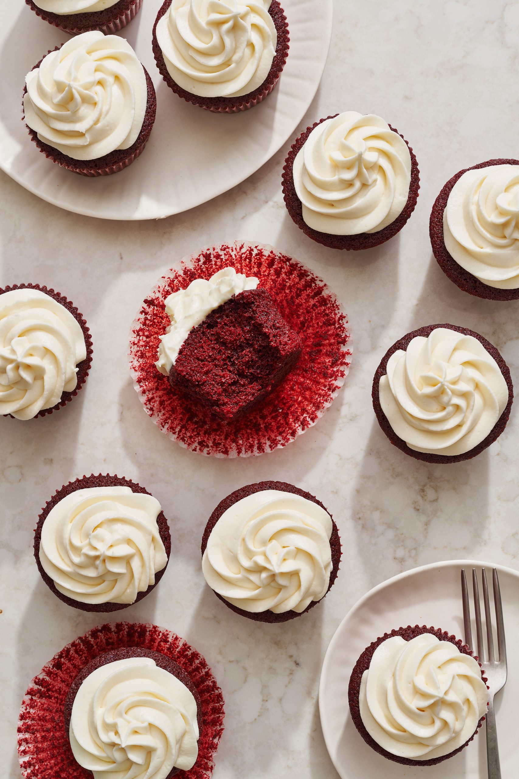 an assortment of red velvet cupcakes, iced with swirls of cream cheese frosting, on white plates ready to serve.