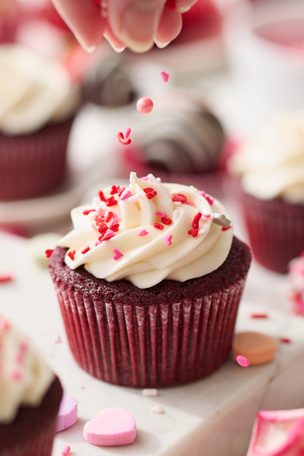 cute Valentine's Day sprinkles being placed on a frosted red velvet cupcake.