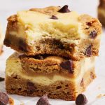 stack of chocolate chip cookie cheesecake bars, top bar with a bite taken out