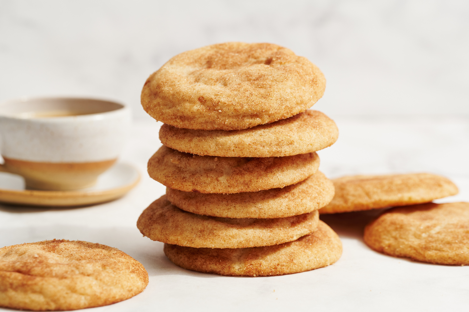 a tall stack of snickerdoodle cookies, with more in the background plus a cup of coffee.