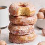 a stack of four glazed donuts with the top donut with a bite taken out.