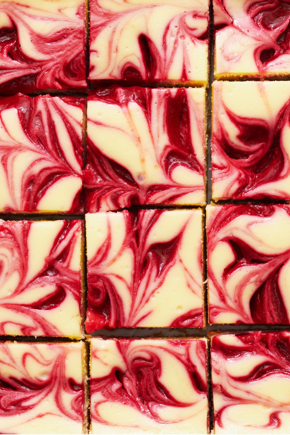 closeup of 12 slices of cheesecake bars, showing their vibrant red swirls of raspberry. 