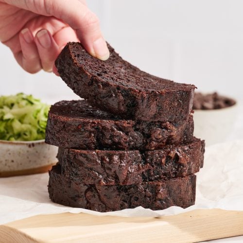 four slices of chocolate zucchini bread stacked, with a hand taking the top slice.