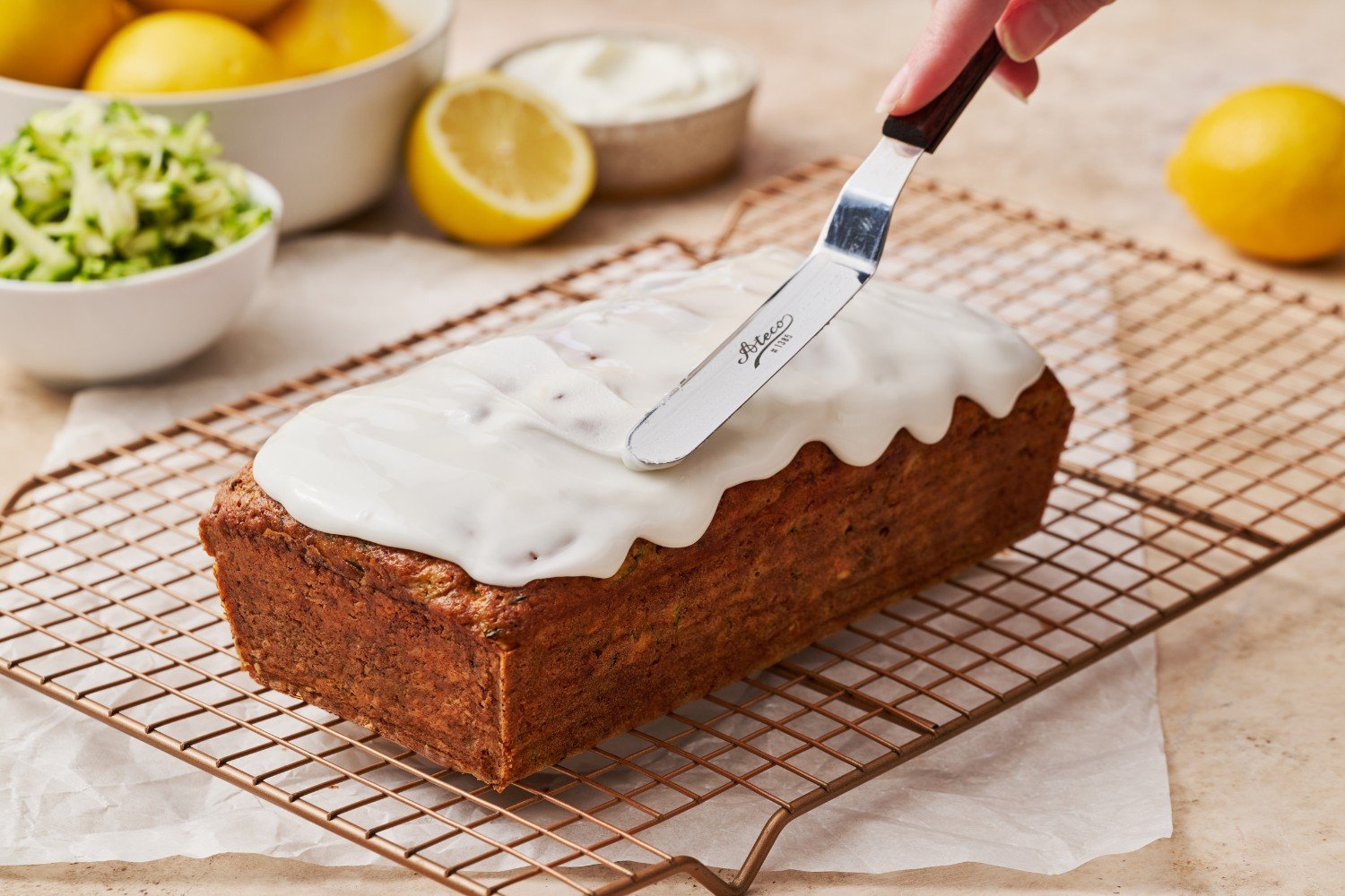 the full loaf of zucchini bread being iced with a lemon icing, using an offset spatula.